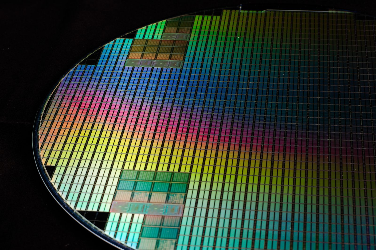 Enrique Jiménez / Wikimedia Commons · CC BY-SA 2.0 A polished silicon wafer patterned with integrated-circuit dies, catching rainbow diffraction
