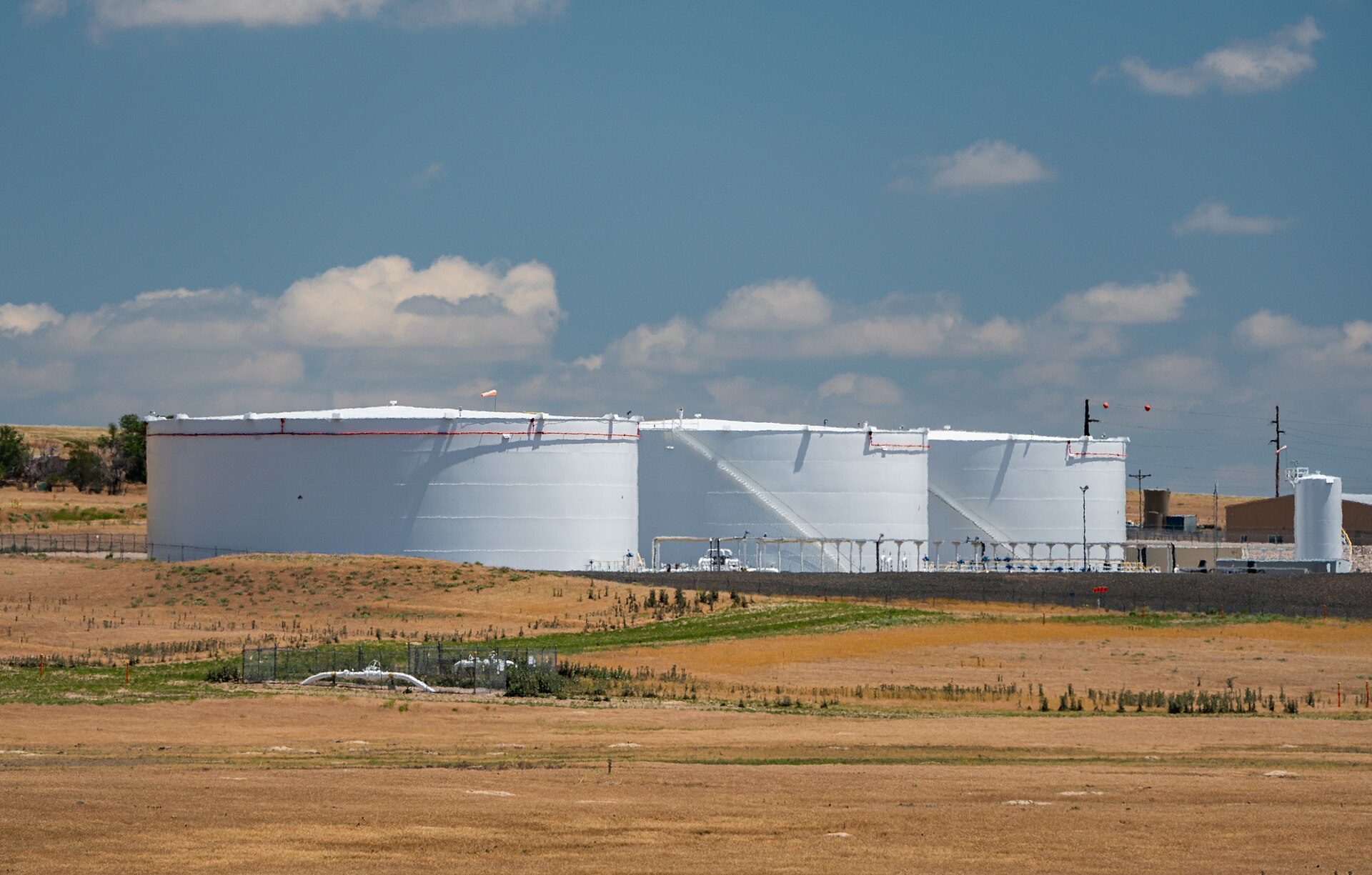 An aerial view of dozens of large circular crude-oil storage tanks arranged across a tank farm.