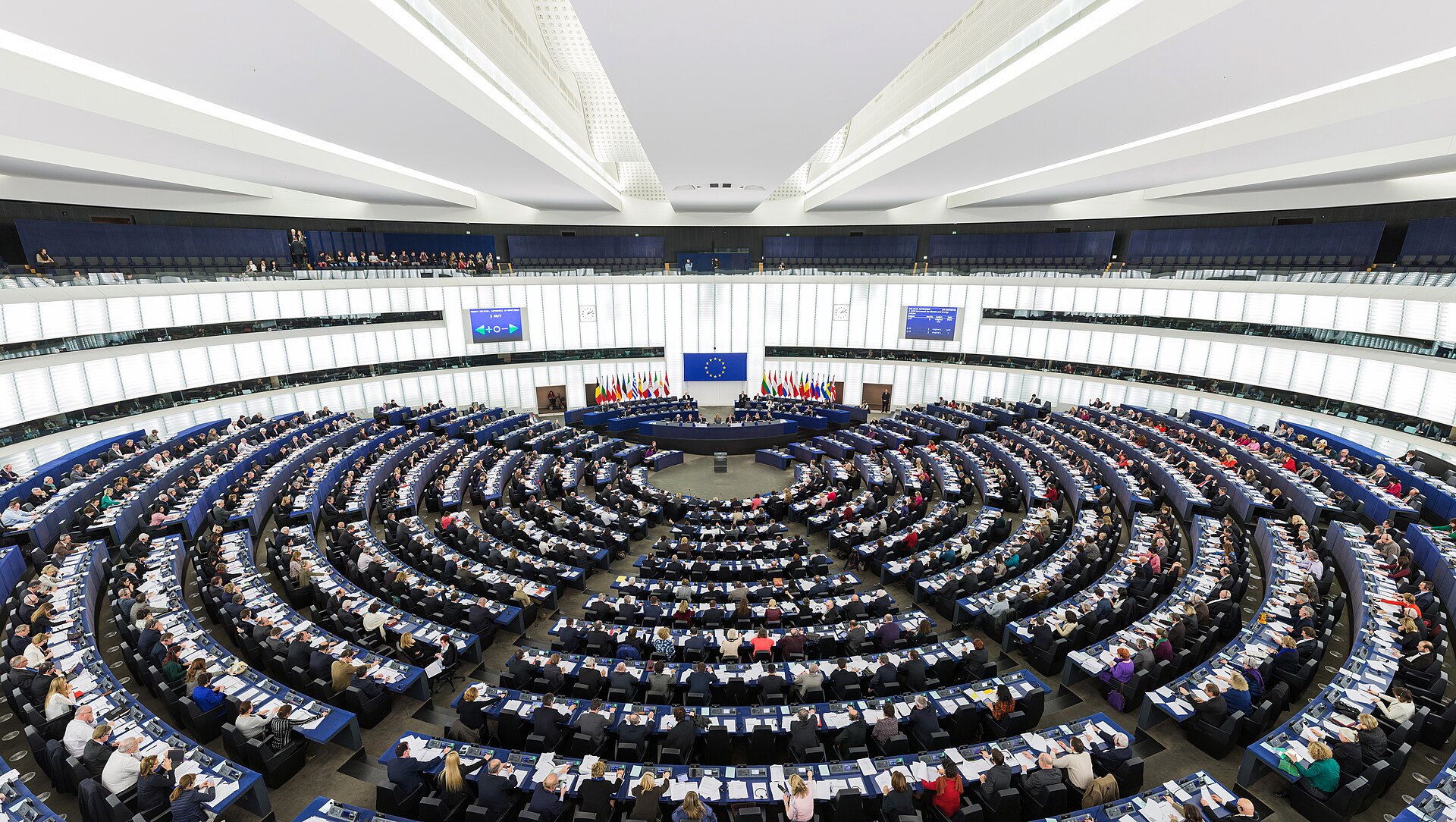 The large semicircular debating chamber of the European Parliament in Strasbourg, tiers of desks curving toward a central rostrum.