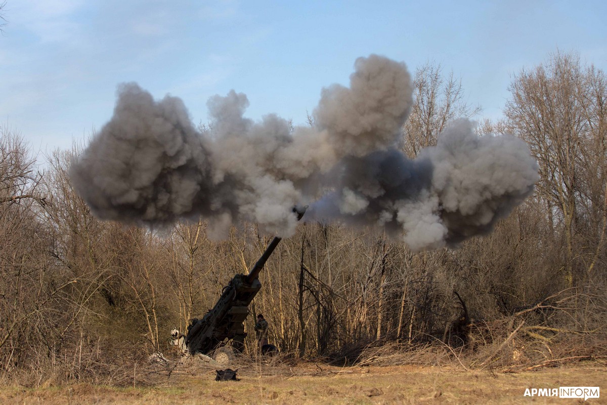 Ukrainian soldiers firing an M777 towed howitzer, the gun recoiling amid smoke.